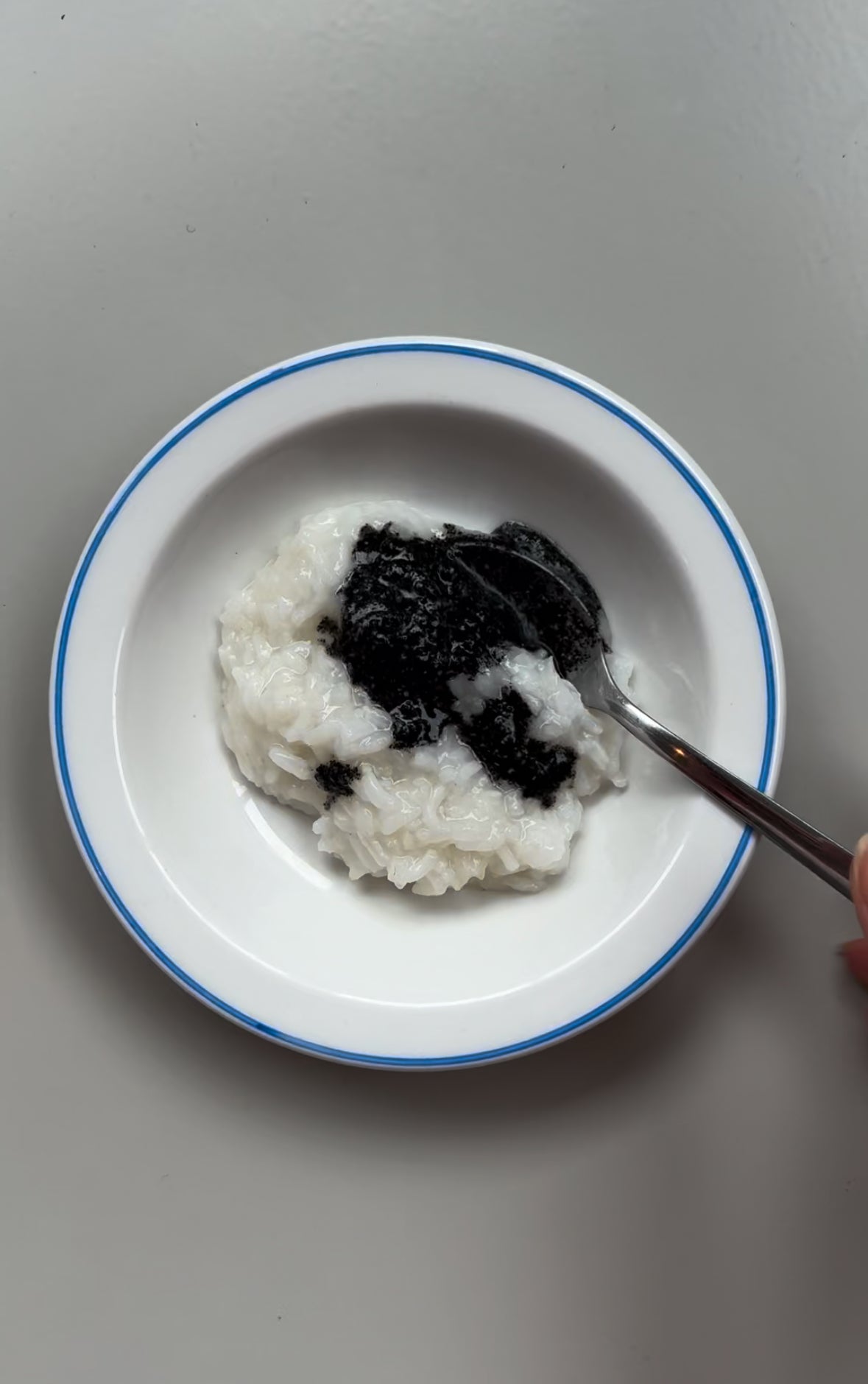 A bowl of Honey Congee with Black Sesame, with the congee and sesame seeds visible on the surface of the bowl.