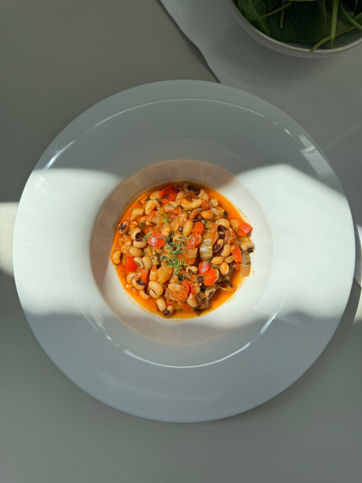 A bowl of black-eyed pea stew served on a white plate, with a shadow falling over the plate.