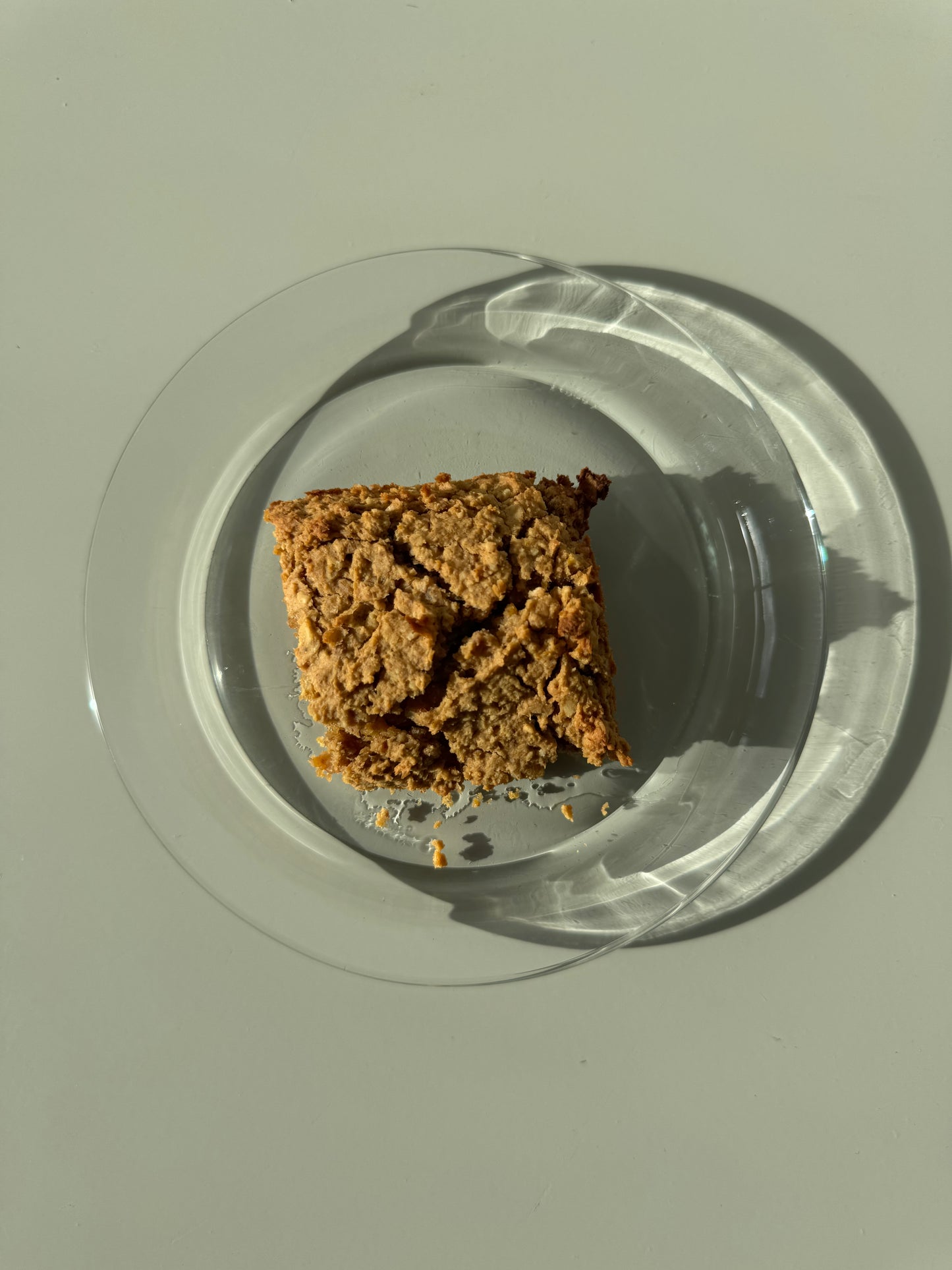 A single blondie square in a clear glass plate with a soft, fudgy texture and a peanut butter color.