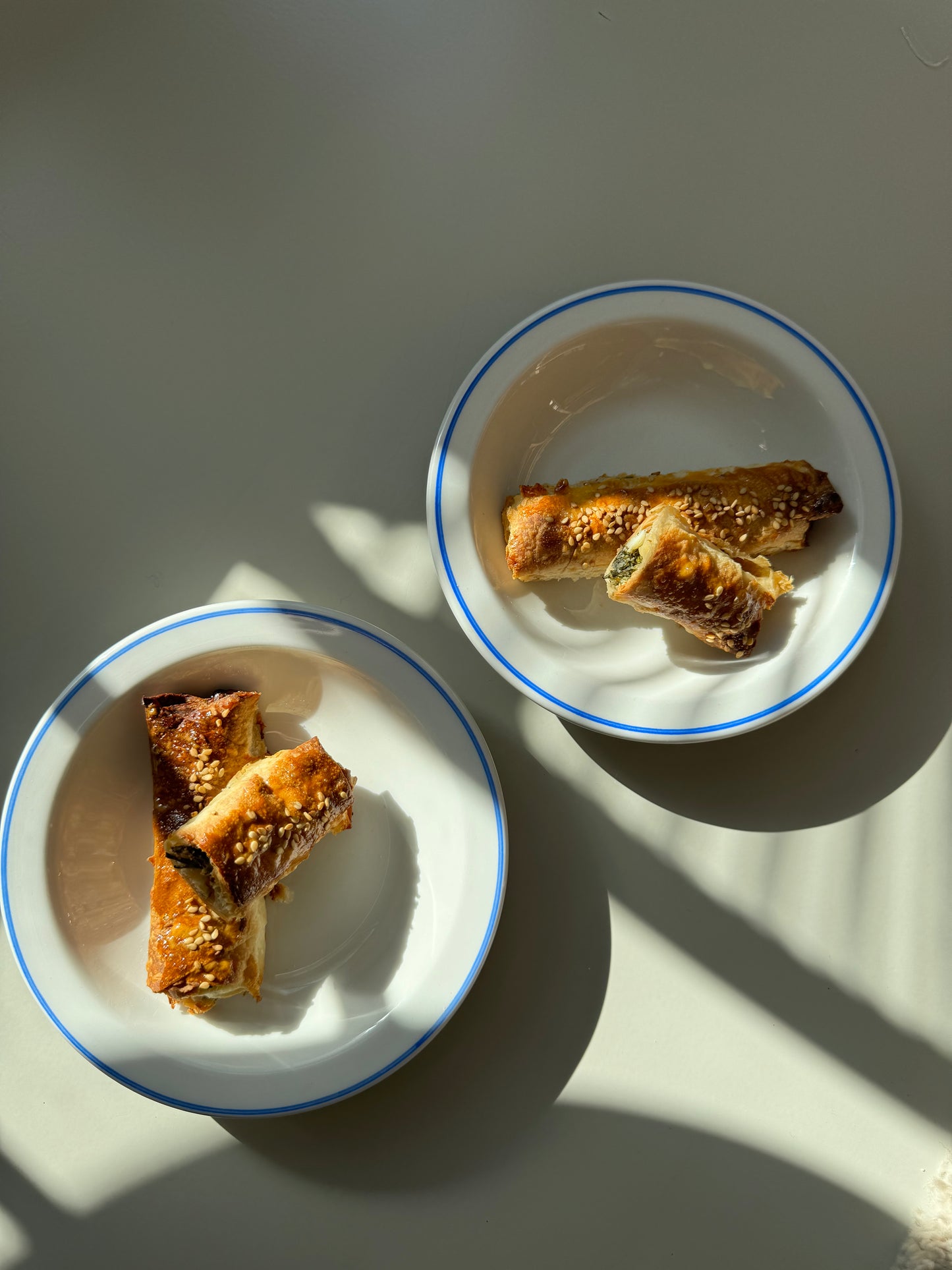 A double borek with feta cheese and parsley on a round white plate with a blue rim, placed on a surface with a shadow pattern.