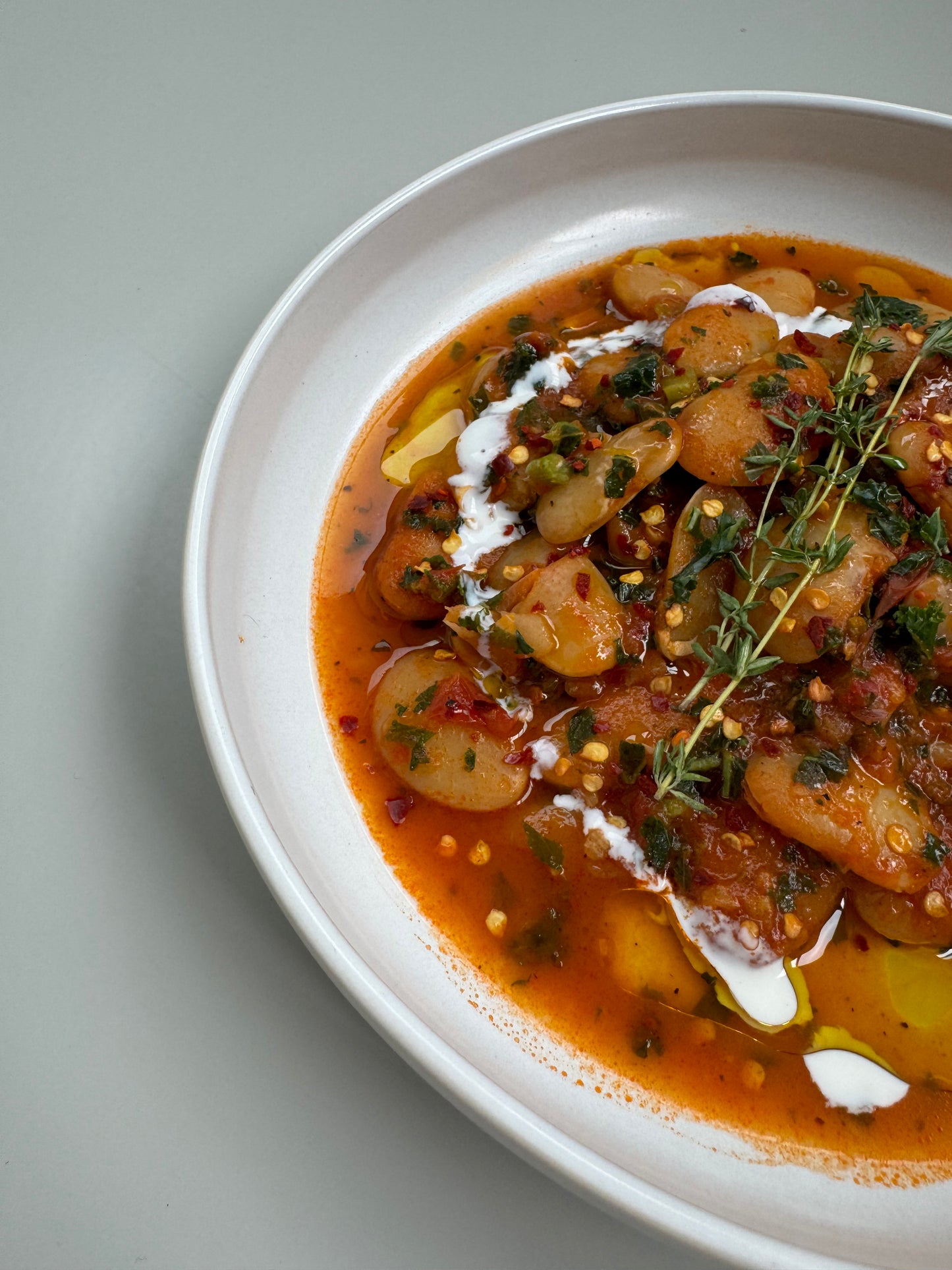 A bowl of creamy tomato butter beans with fresh kale, served on a white plate.