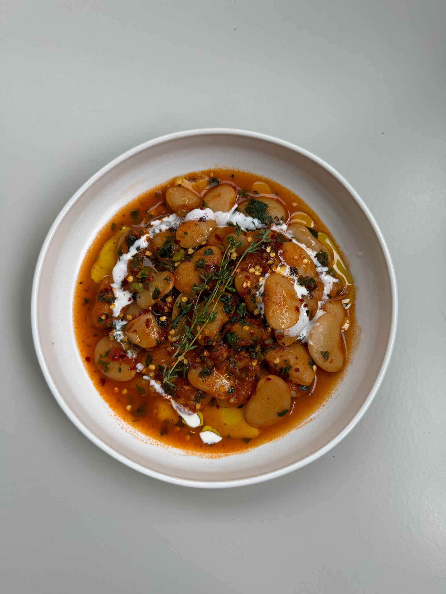 A bowl of creamy tomato butter beans with fresh kale, served on a white plate and cream.