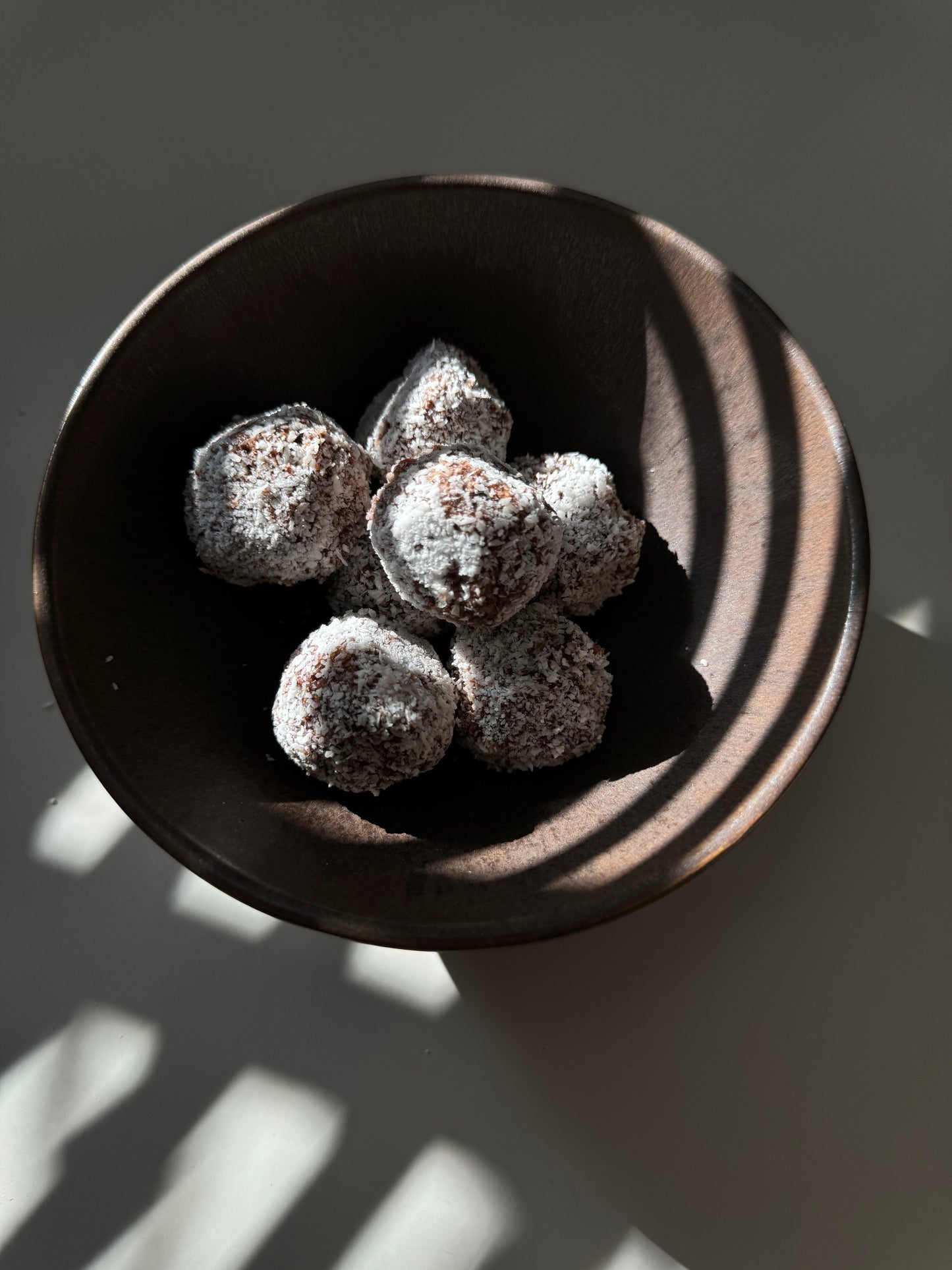 A plate of round bliss balls made of oats, almonds, dates, and coconut, sprinkled with cinnamon and coconut flakes in the shade