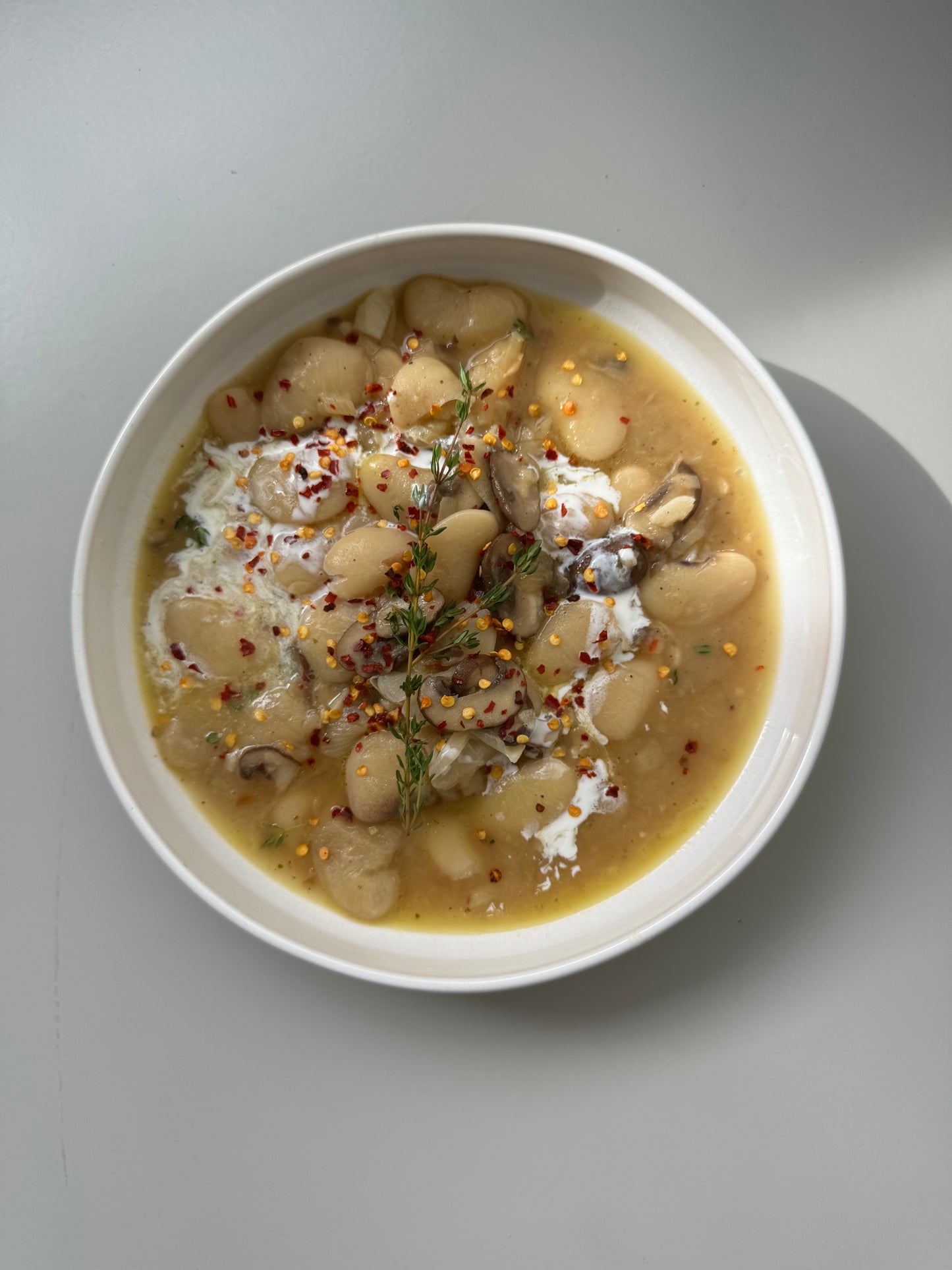 A bowl of prepared caramelized onion butter beans meal, garnished with fresh parsley and a piece of caramelized onion, on a light background.