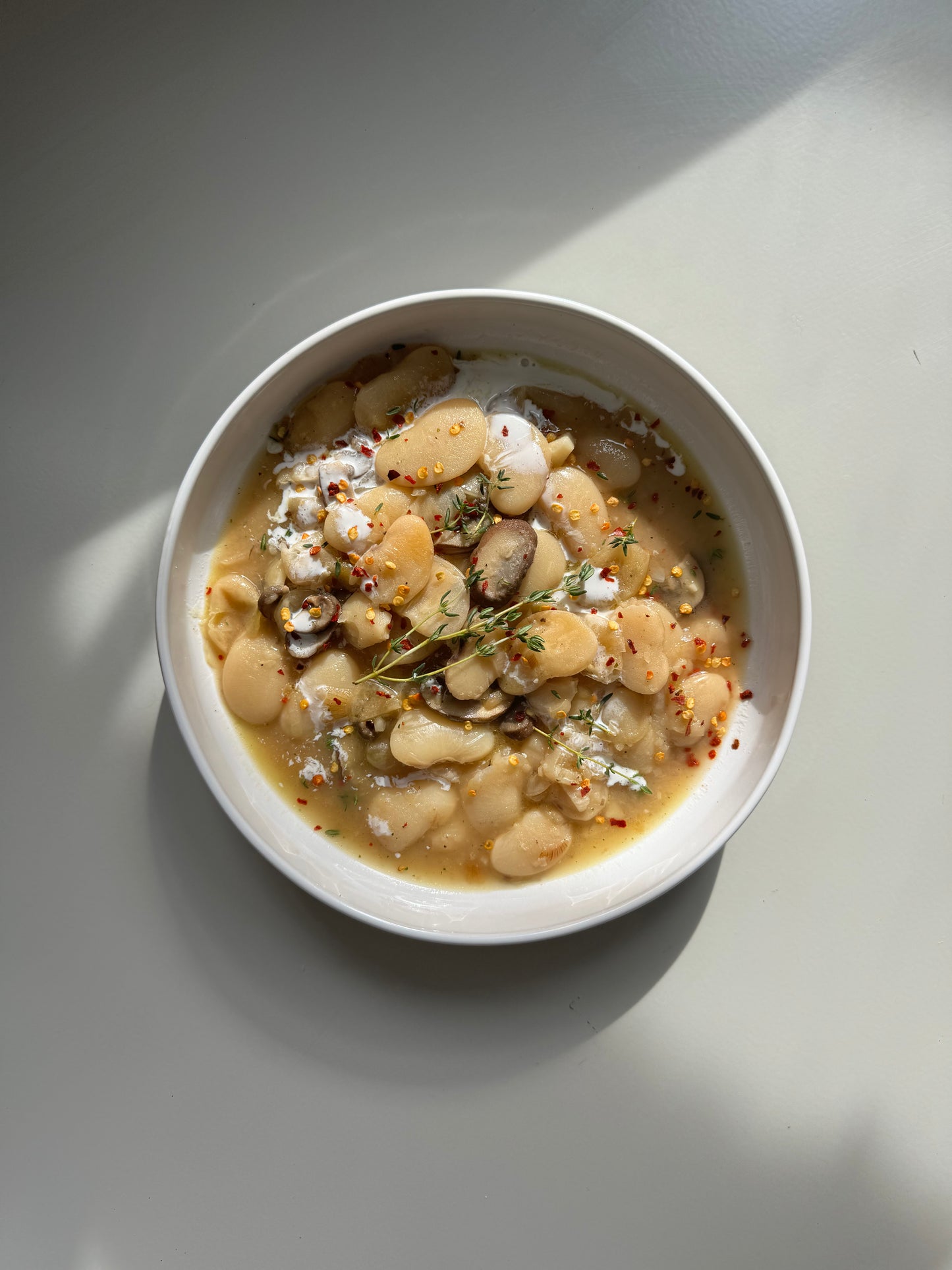 A bowl of prepared caramelized onion butter beans meal, garnished with fresh parsley and a piece of caramelized onion, on a light background.