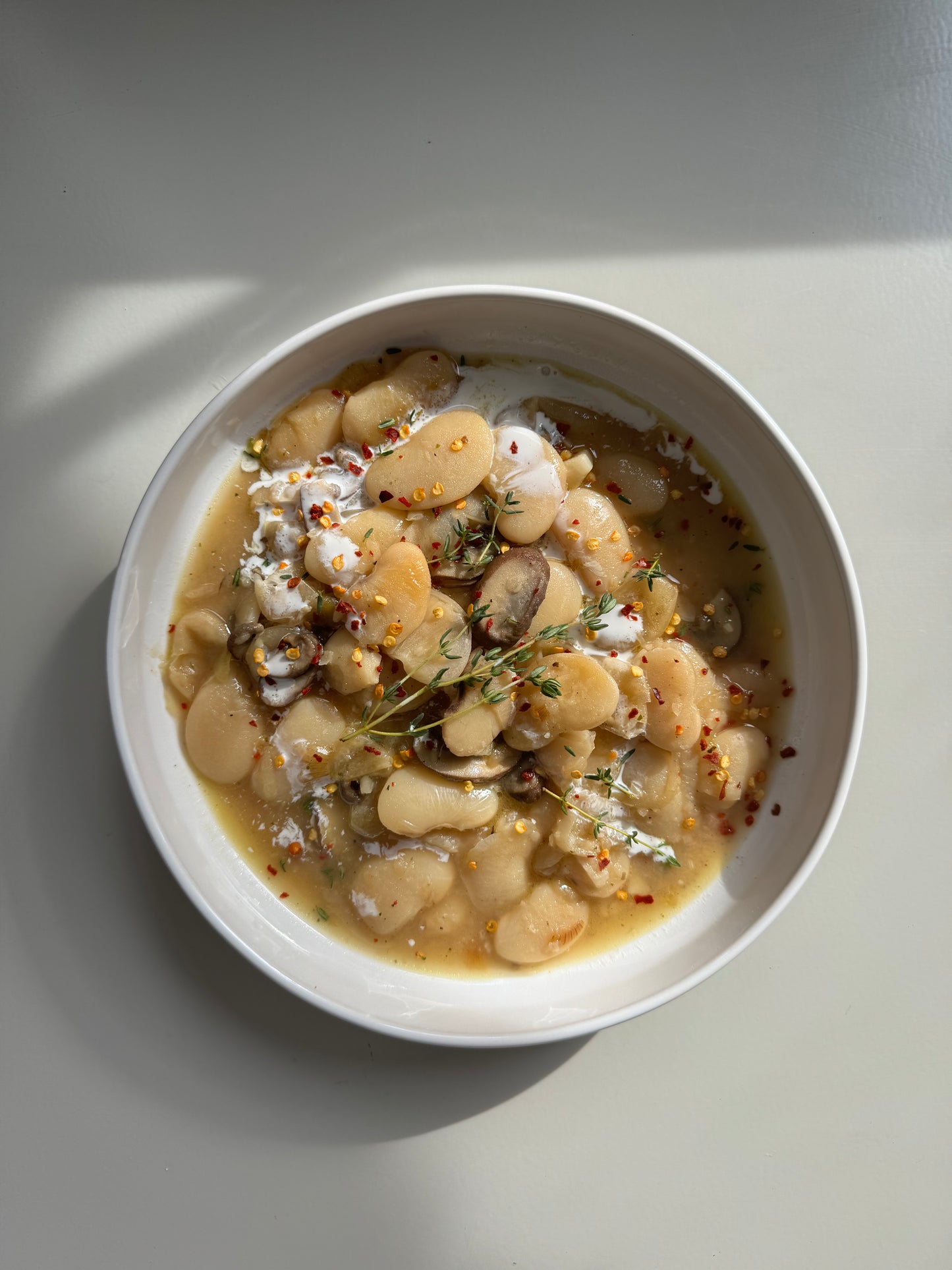 A bowl of prepared caramelized onion butter beans meal, garnished with fresh parsley and a piece of caramelized onion, on a light background.