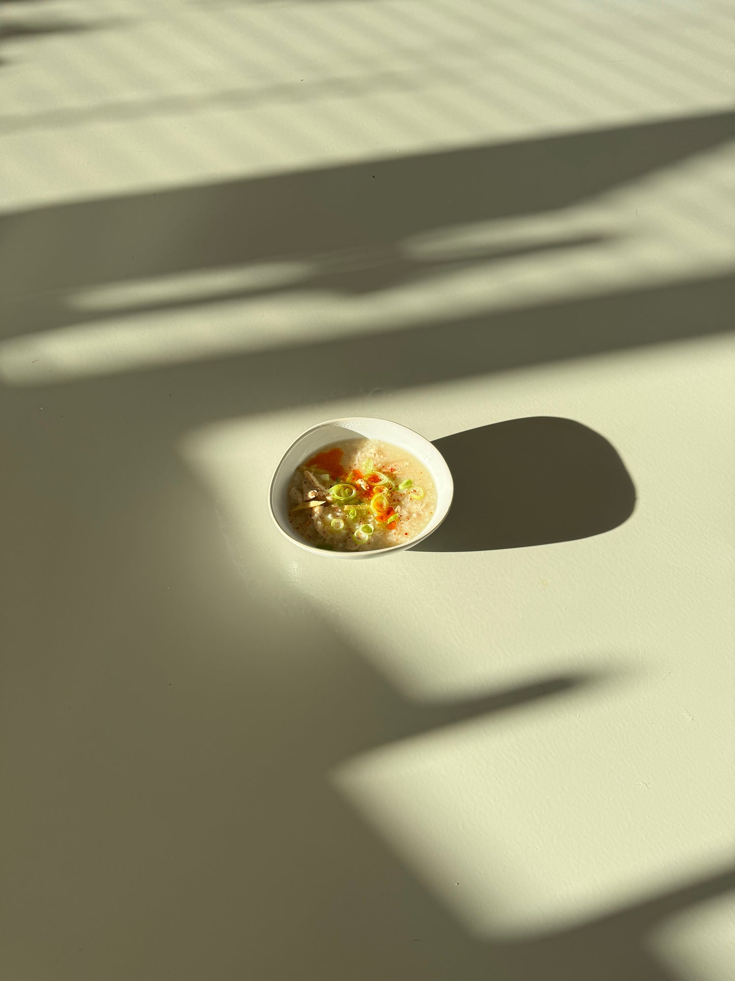 A bowl of chicken congee with visible carrots and celery, placed on a neutral background.