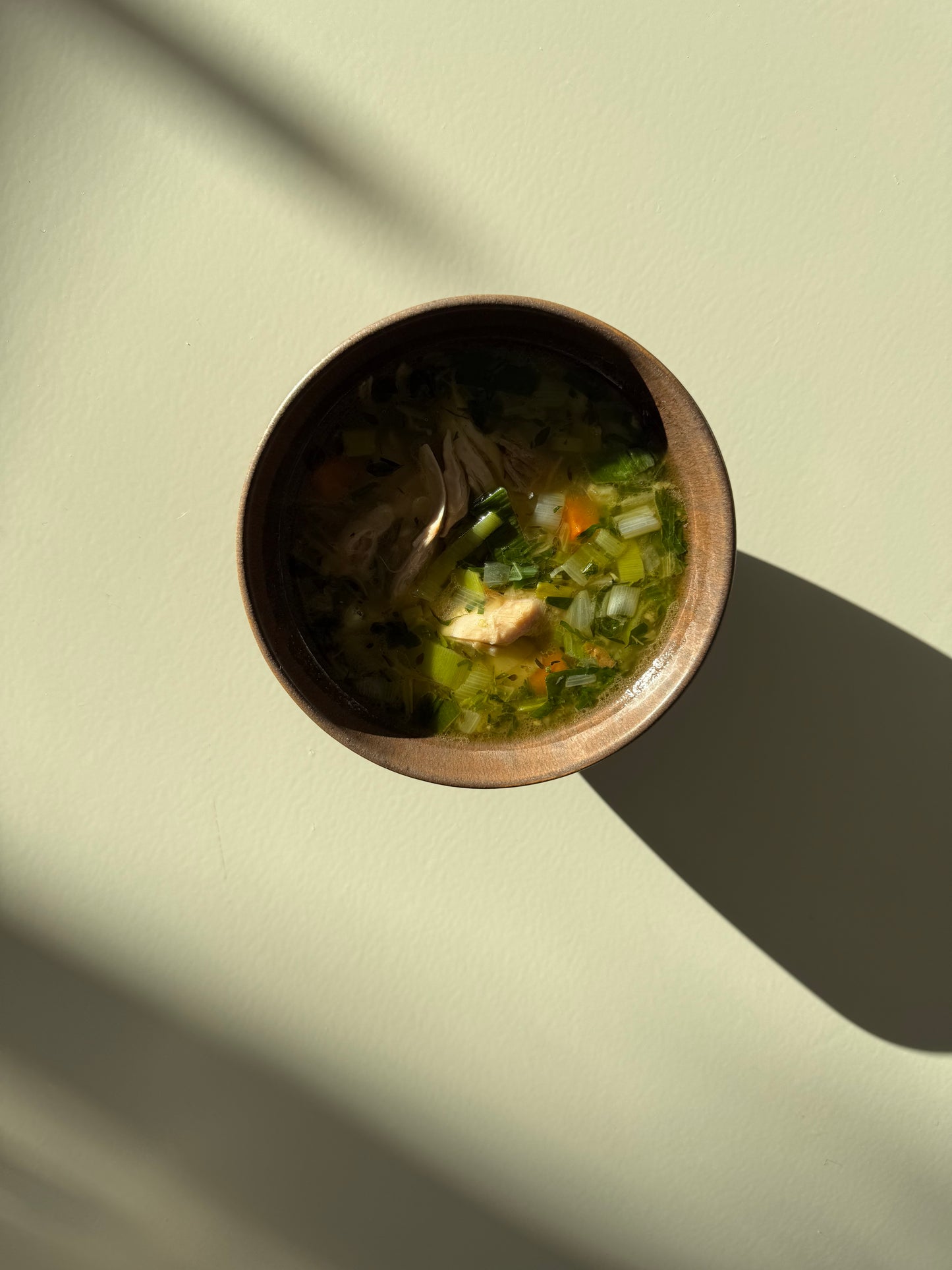 A bowl of chicken soup with visible carrots and celery, placed on a neutral background.
