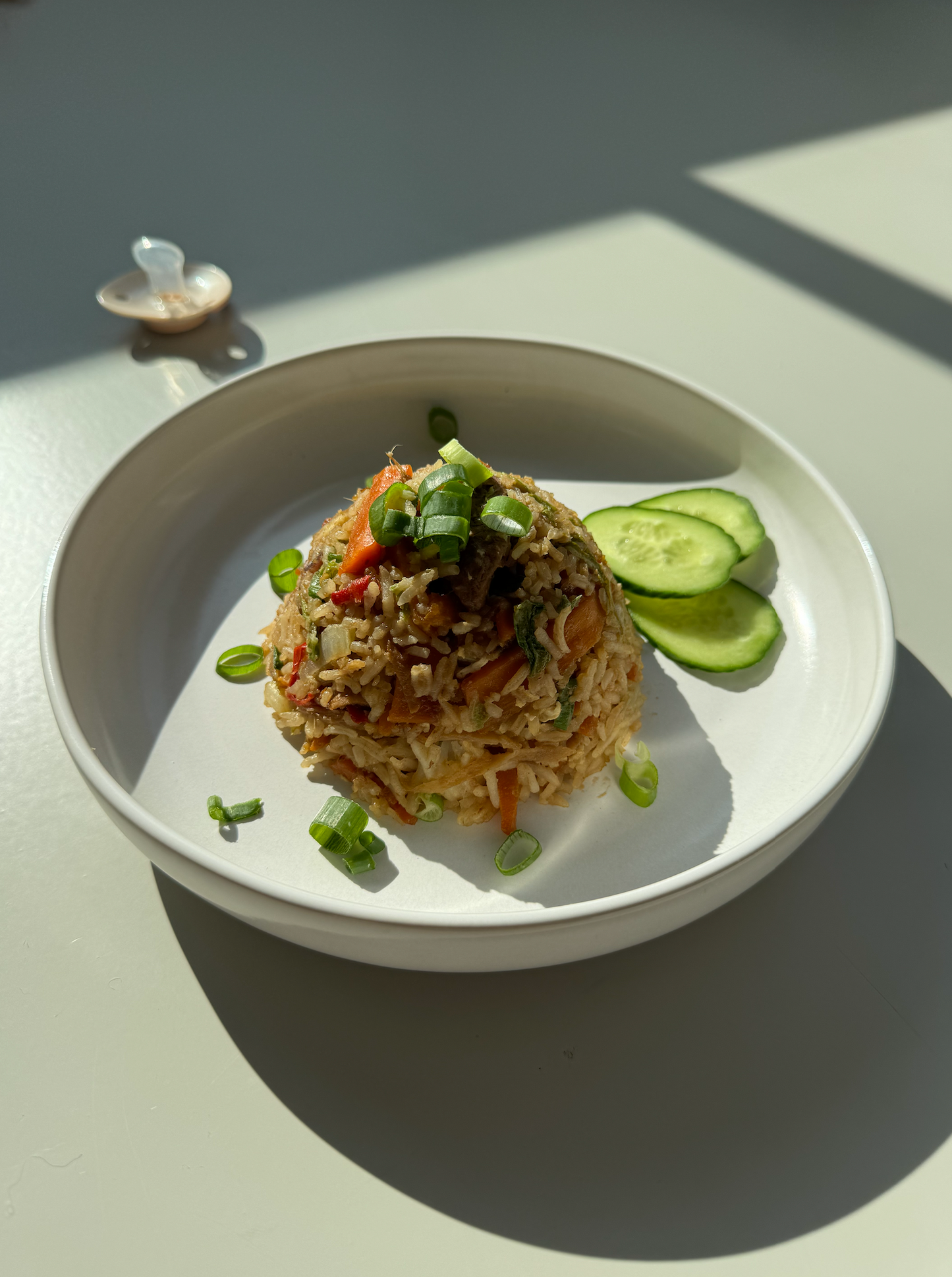 Ginger fried rice with green vegetables and a pacifier in the back. Shadows on plate