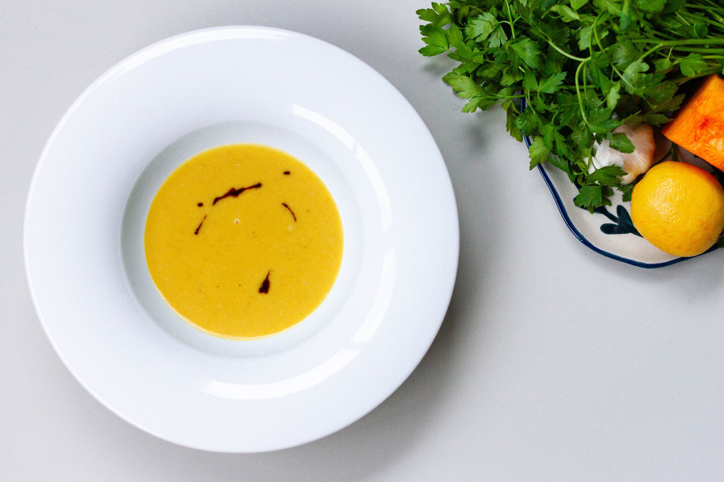 A bowl of creamy squash and red lentils soup next to a scattering of red lentils on a light surface, with a shadow falling over part of the image.