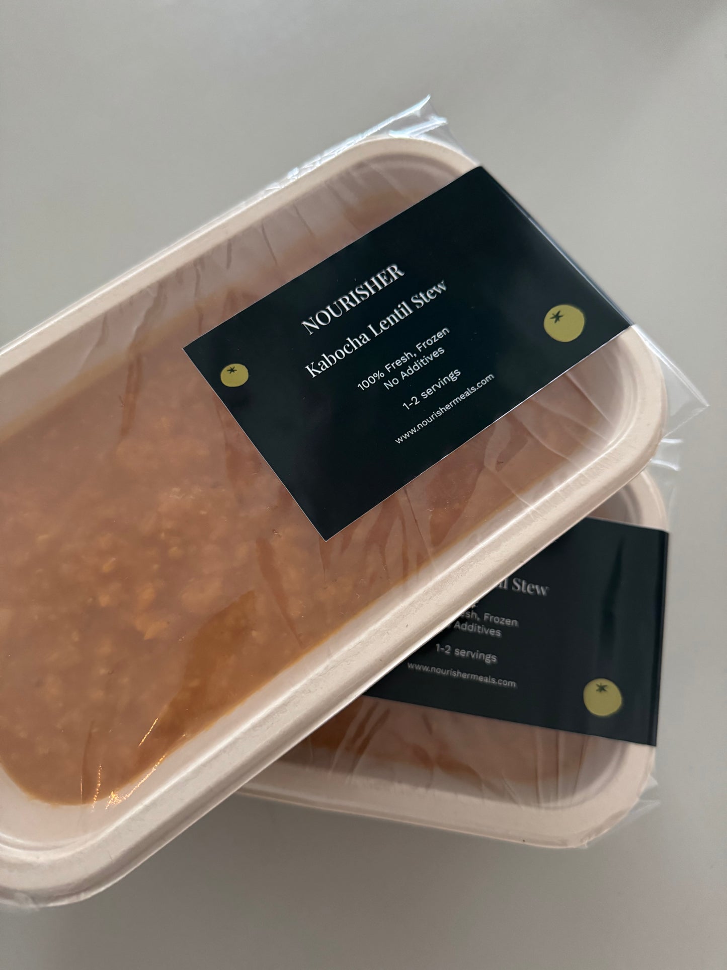 Two packaged units of Kabocha Lentil Stew on a light background, one package is in the foreground and the other in the background.