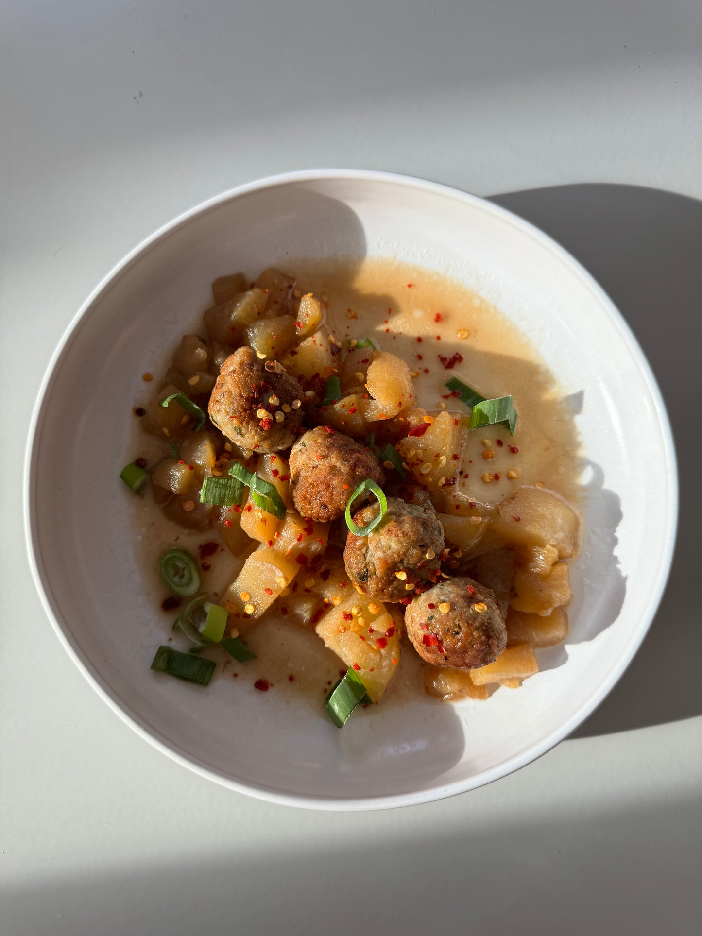 A bowl of ginger chicken meatballs in pear sauce, garnished with basil leaves.