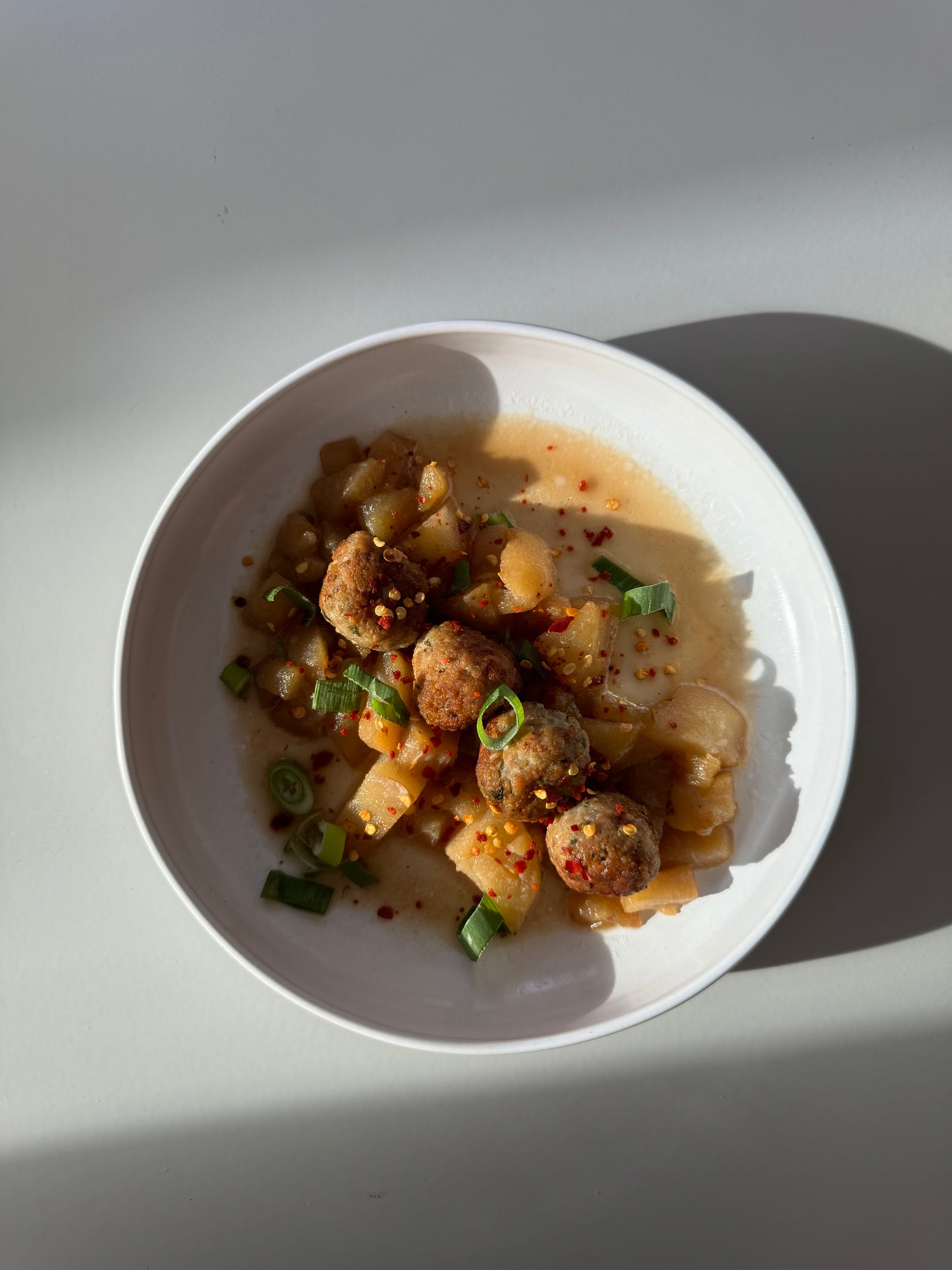 A bowl of ginger chicken meatballs in pear sauce, garnished with basil leaves.