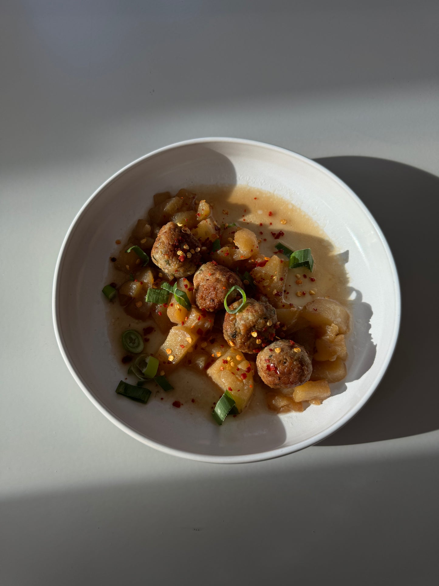 A bowl of ginger chicken meatballs in pear sauce, garnished with basil leaves.