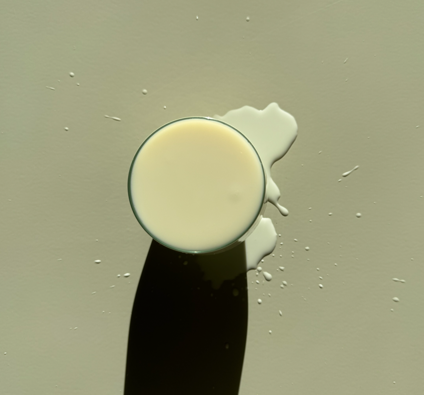 A glass of milk with a shadow cast on a beige background.