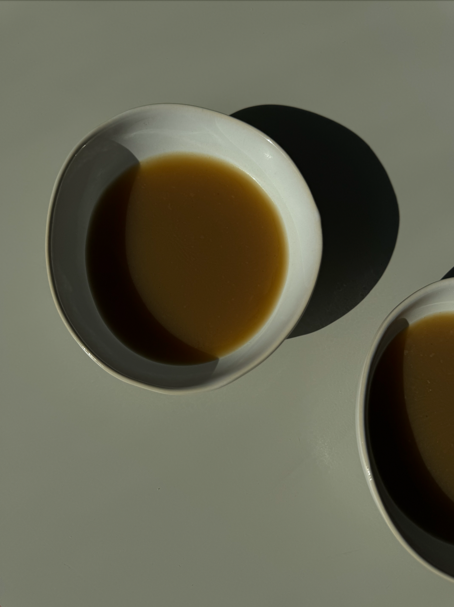 A fresh bowl of Shiitake Immune Boost broth with visible leeks, a lemon wedge, and other ingredients in the background.