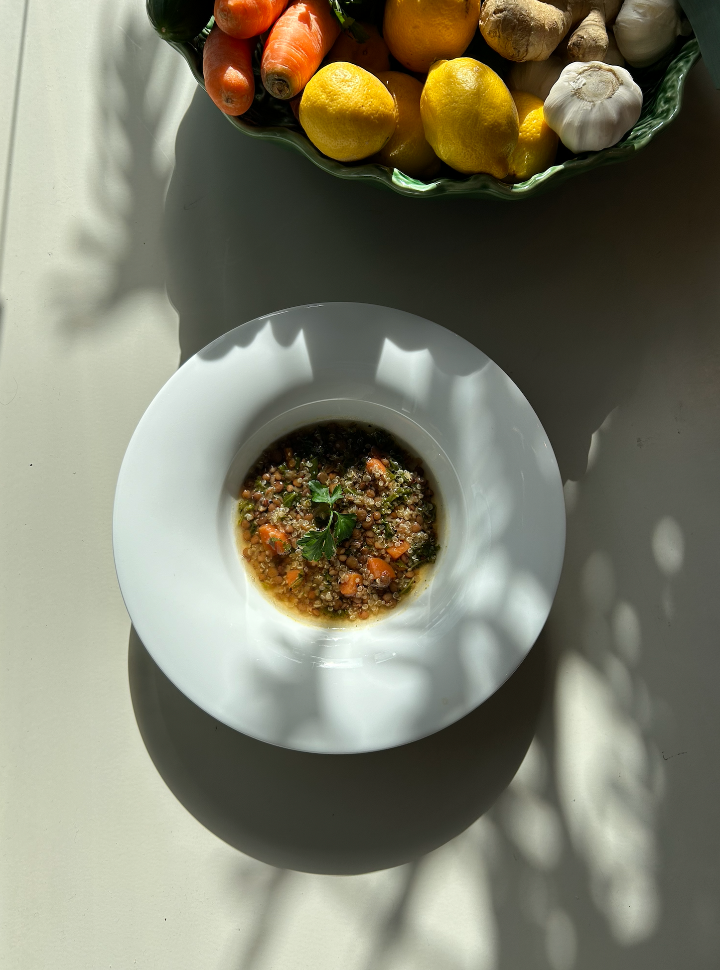 A bowl of quinoa, lentils, and greens soup on a white plate with a red and white checkered napkin on top, placed on a table with lighting overhead.