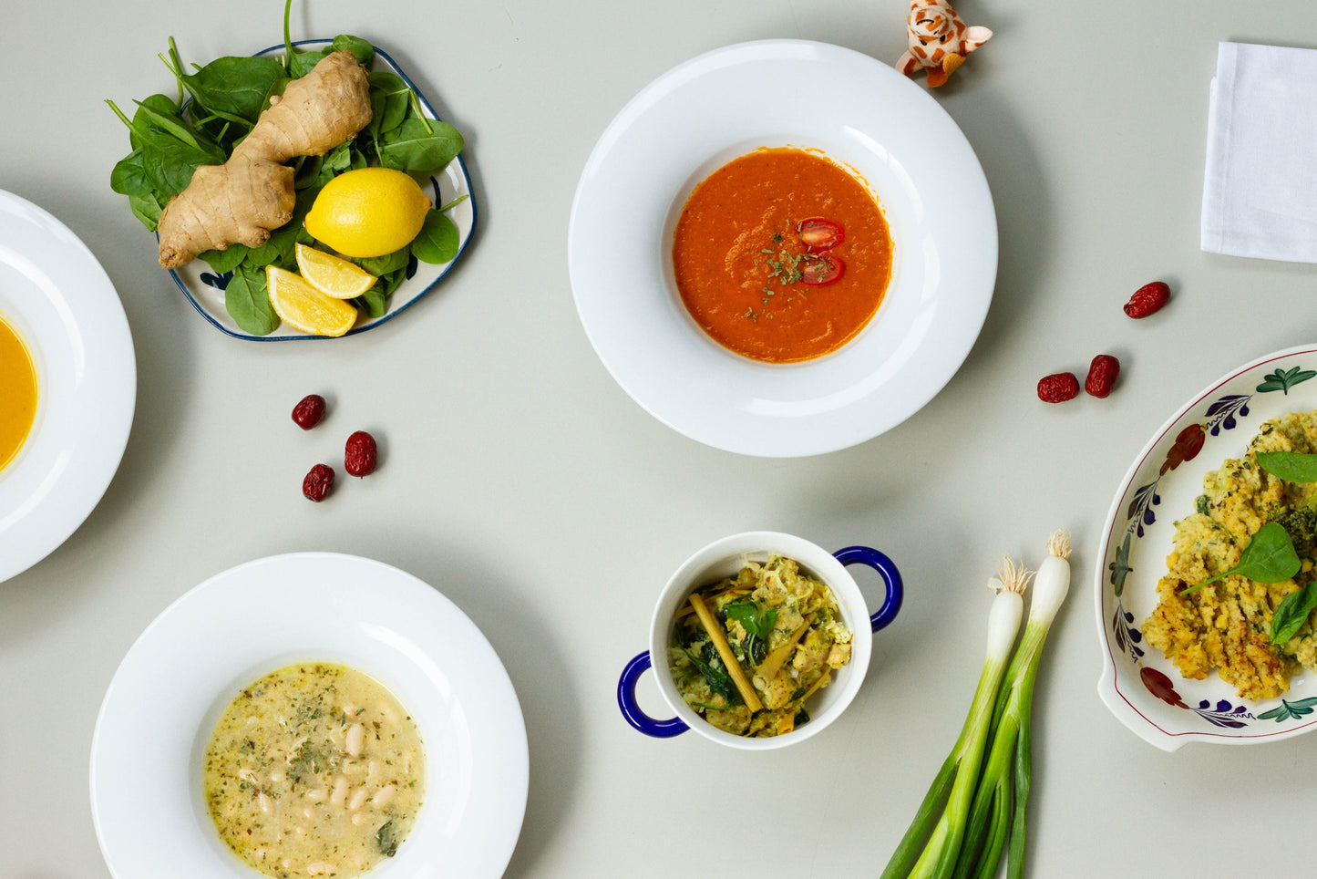 A bowl of roasted tomato soup with a garnish of basil leaves on a white plate, with a shadow falling over the plate. and more delicious food