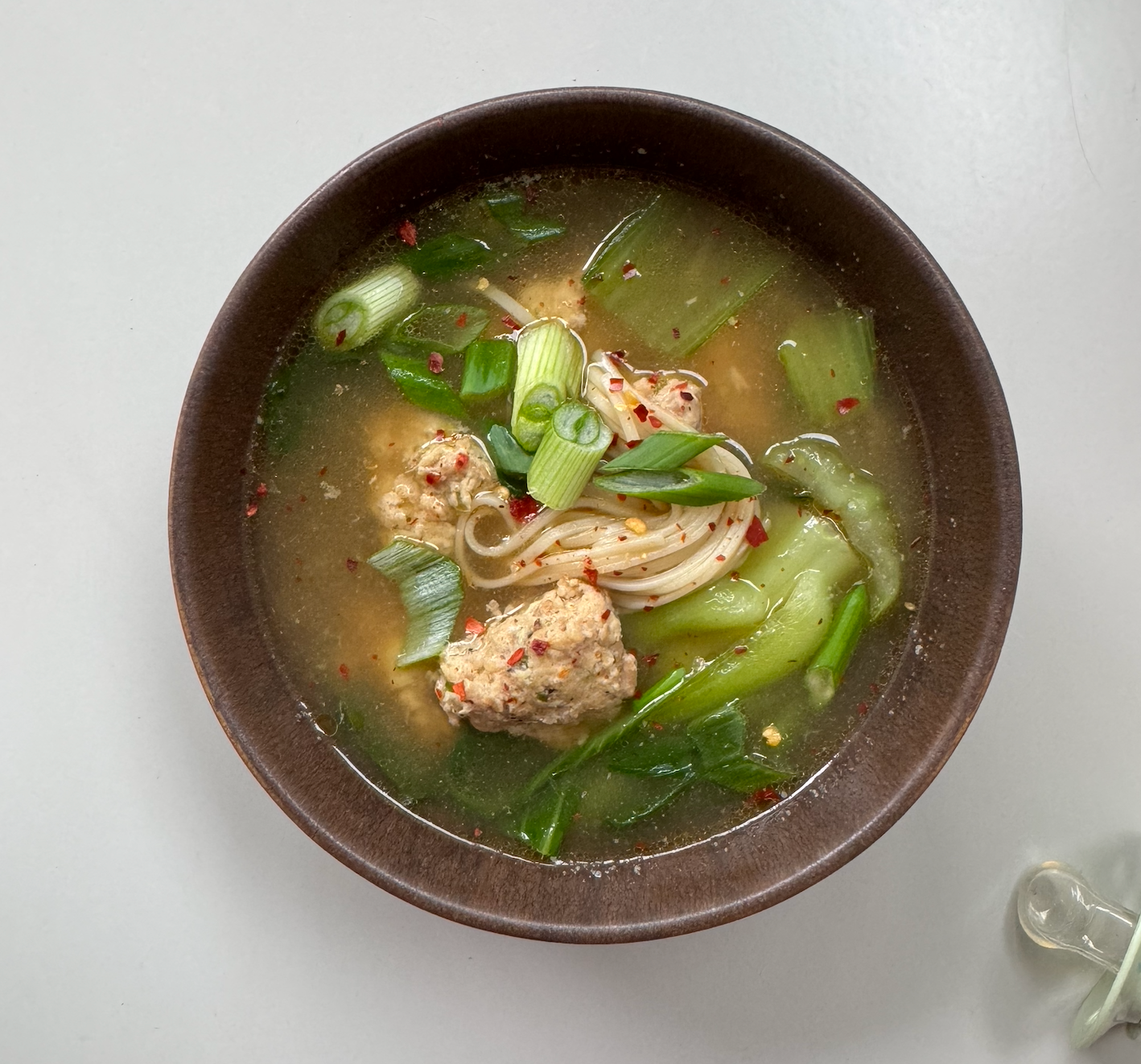 Bowl of soup with noodles, vegetables, and meatballs on a white background