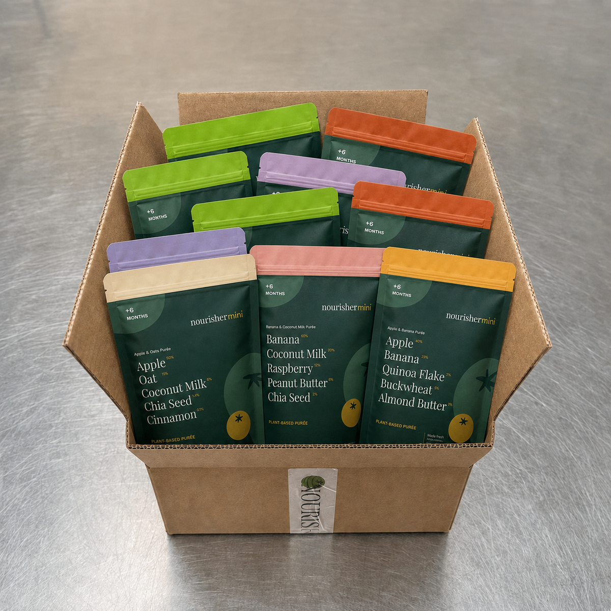A cardboard box filled with multiple pouches of nourishermin protein powder mixes, arranged on a gray metal surface. The front pouches show flavors including Apple Gato, Banana Coconut Milk, Peanut Butter Chia Seed, and Almond Butter.