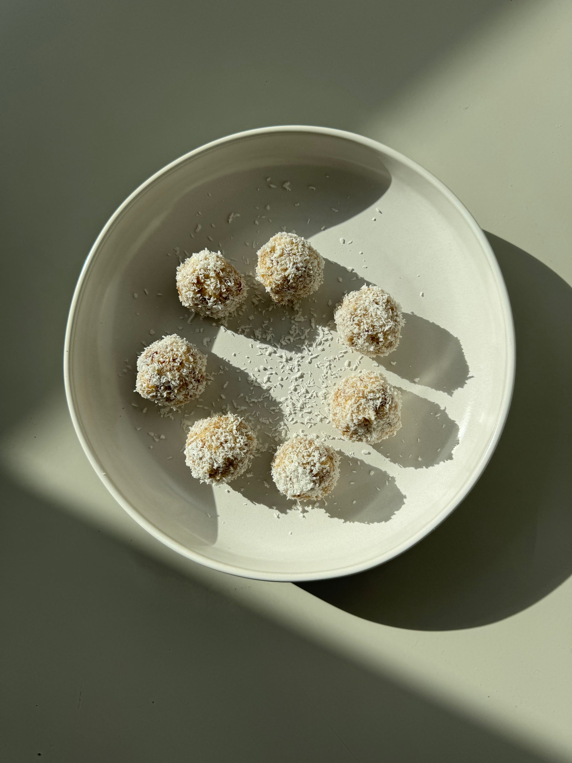 A plate of round bliss balls made of oats, almonds, dates, and coconut, sprinkled with cinnamon and coconut flakes.