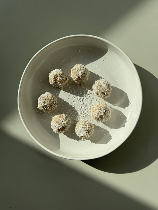 A plate of round bliss balls made of oats, almonds, dates, and coconut, sprinkled with cinnamon and coconut flakes.