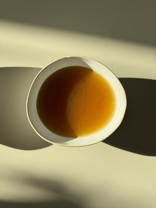 A bowl of clear beef broth placed on a table with natural lighting.