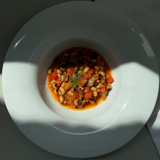 A bowl of black-eyed pea stew served on a white plate, with a shadow falling over the plate.