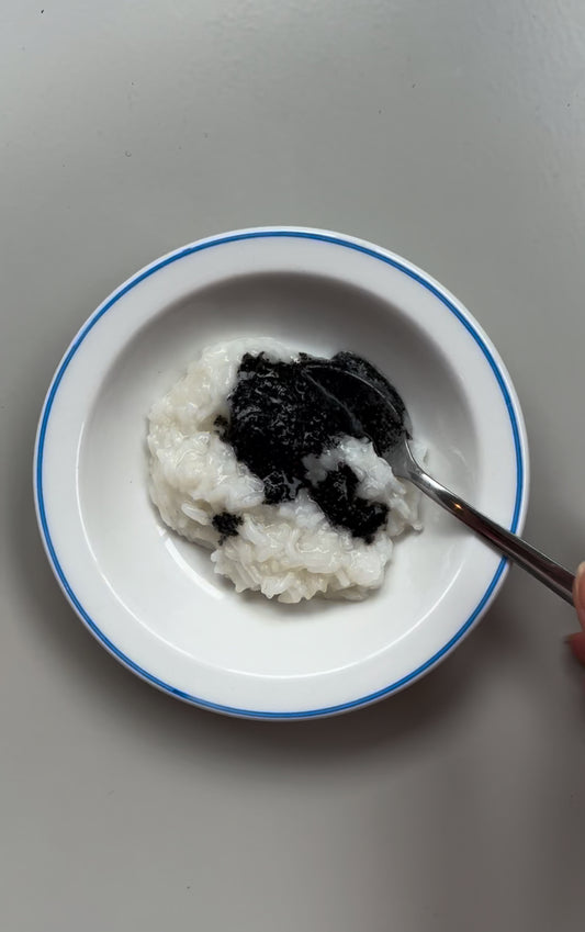 A bowl of Honey Congee with Black Sesame, with the congee and sesame seeds visible on the surface of the bowl.