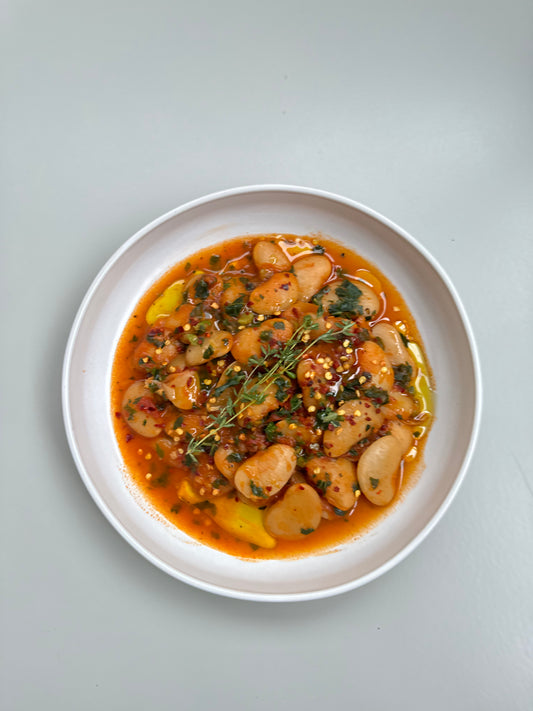 A bowl of creamy tomato butter beans with fresh kale, served on a white plate.