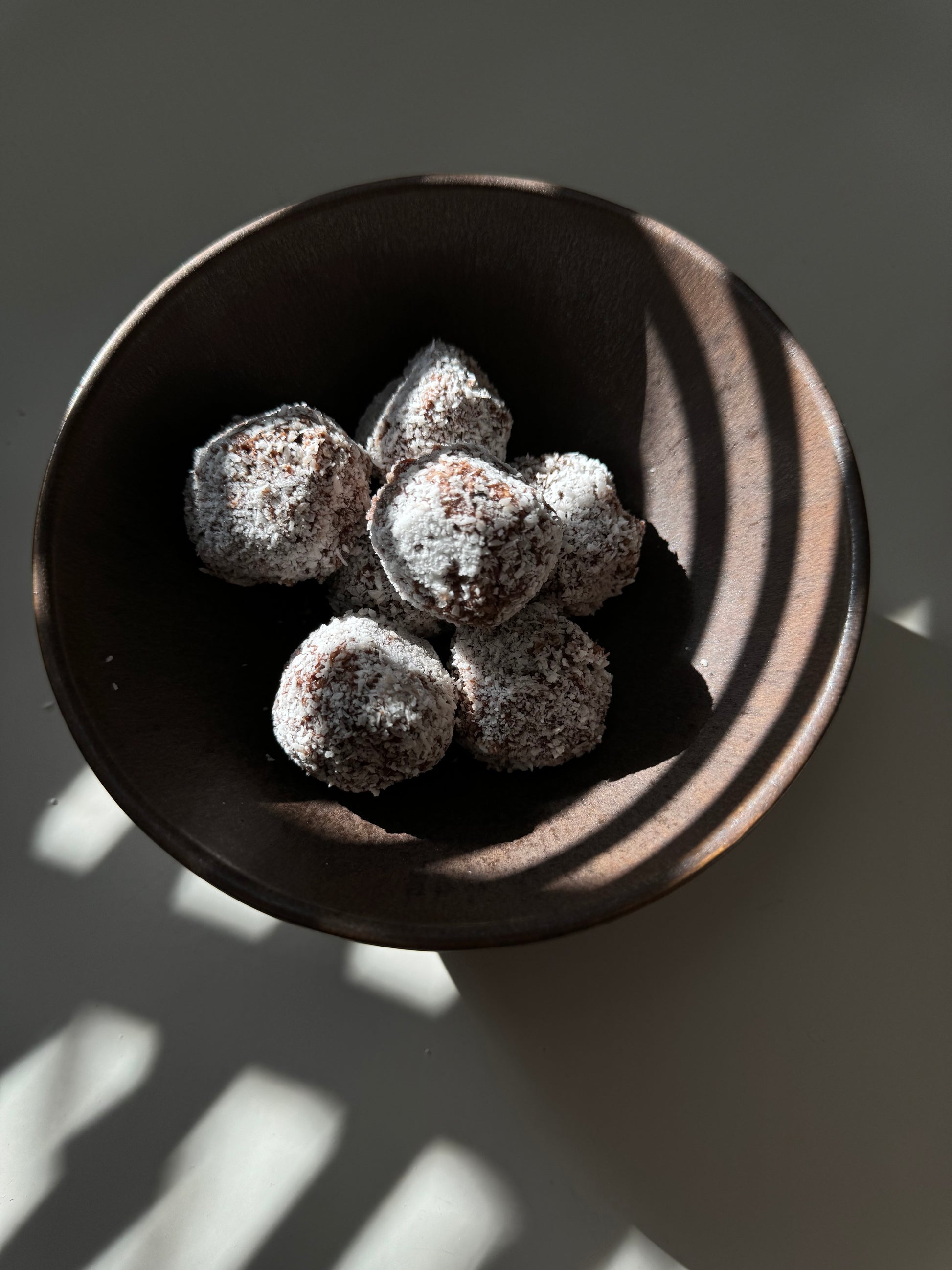 A plate of round bliss balls made of oats, almonds, dates, and coconut, sprinkled with cinnamon and coconut flakes in the shade