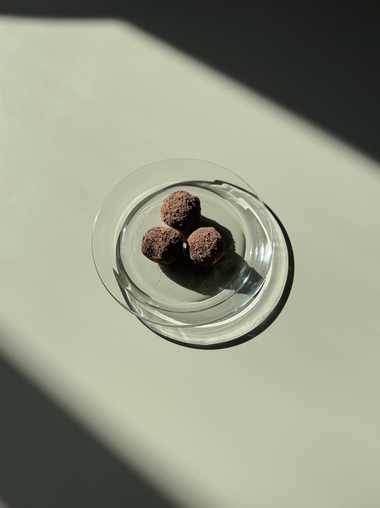 A transparent snack box containing three spherical snacks, placed on a light-colored surface with a shadow cast over part of the image.