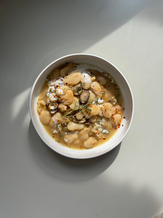 A bowl of prepared caramelized onion butter beans meal, garnished with fresh parsley and a piece of caramelized onion, on a light background.
