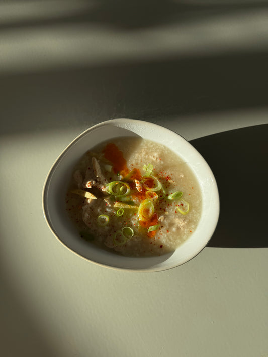 A bowl of chicken congee with visible carrots and celery, placed on a neutral background.