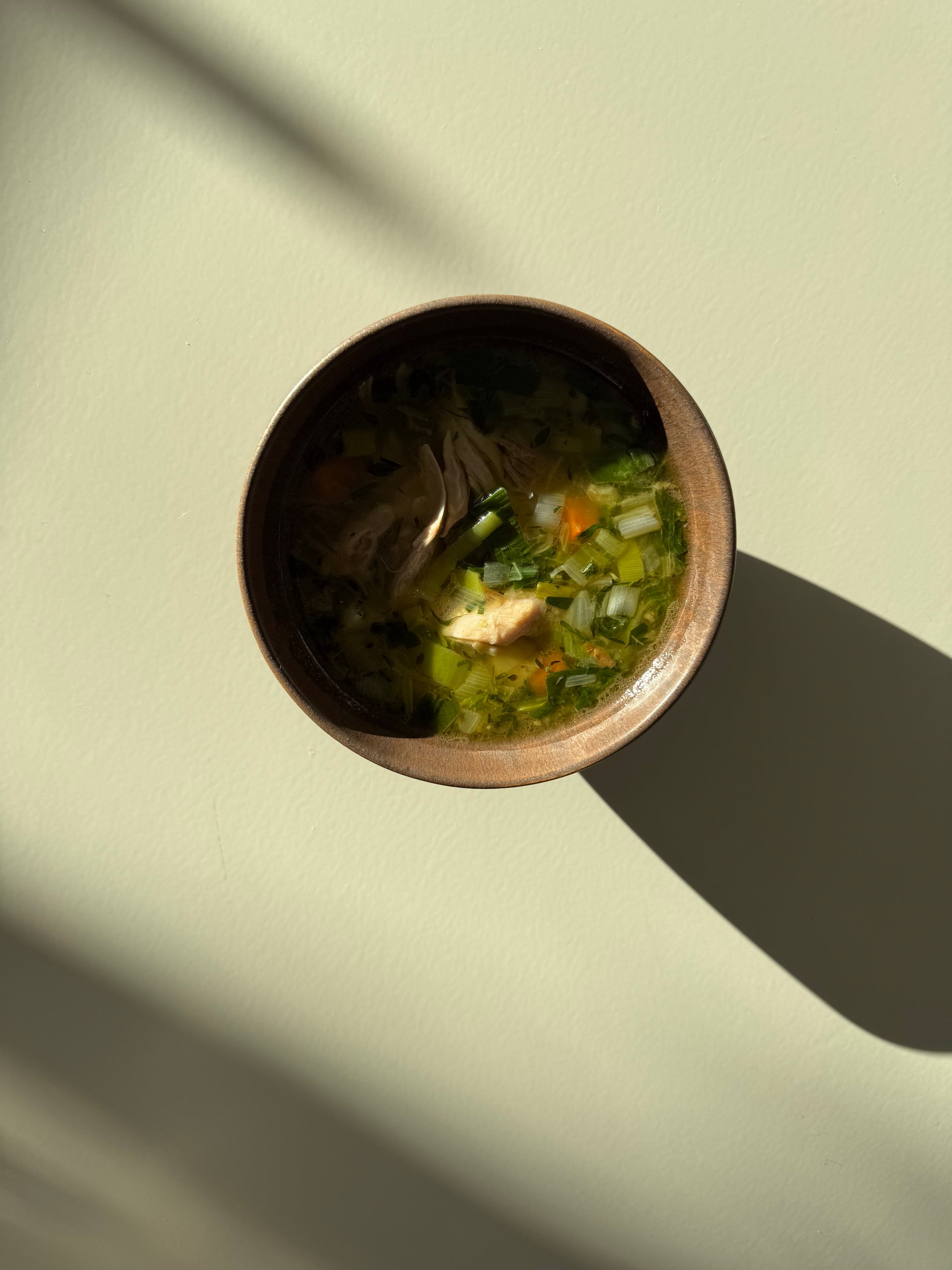 A bowl of chicken soup with visible carrots and celery, placed on a neutral background.