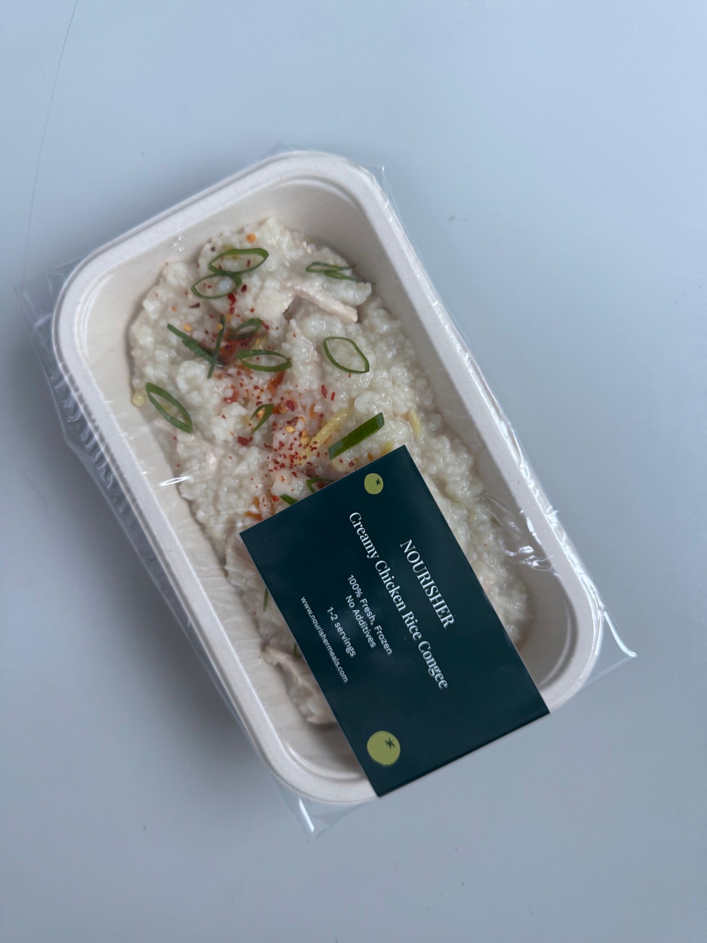 A bowl of chicken congee with visible carrots and celery, placed on a neutral background.