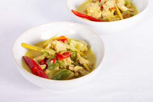 Two bowls of Creamy Lemongrass Coconut Chicken, garnished with herbs and spices, served on a white plate.