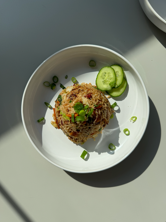 Ginger fried rice with green vegetables and a pacifier in the back. Shadows on plate and cucumber. 