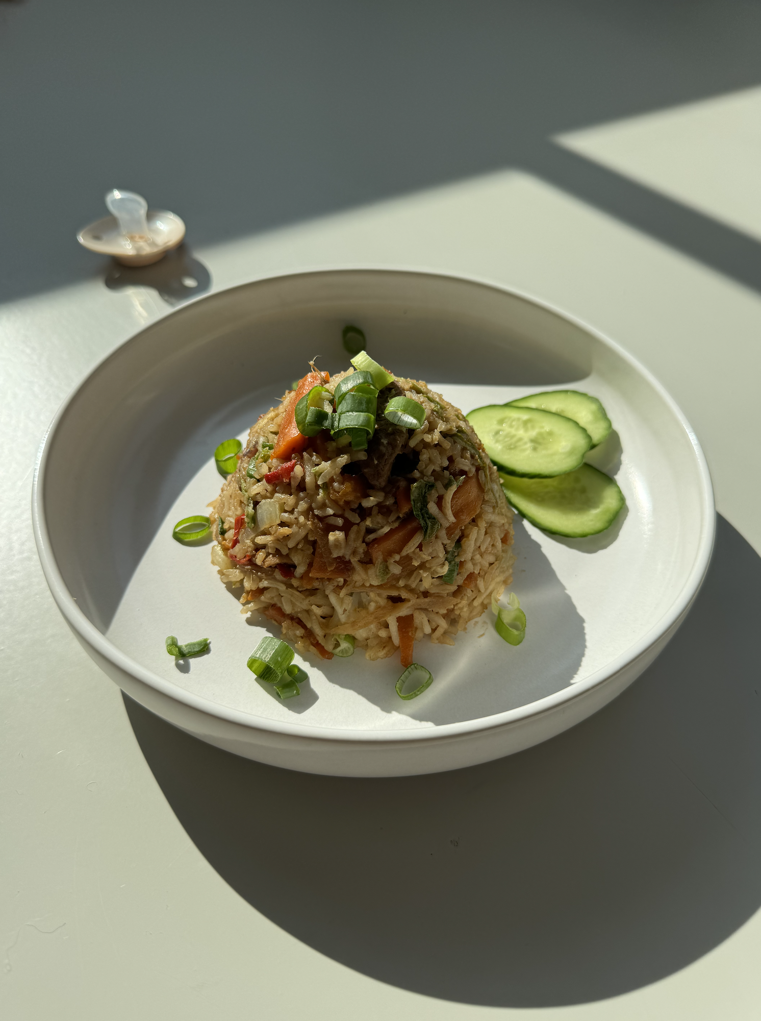 A plate of ginger fried rice with chicken and cucumber on the side, on a bright sunny background.