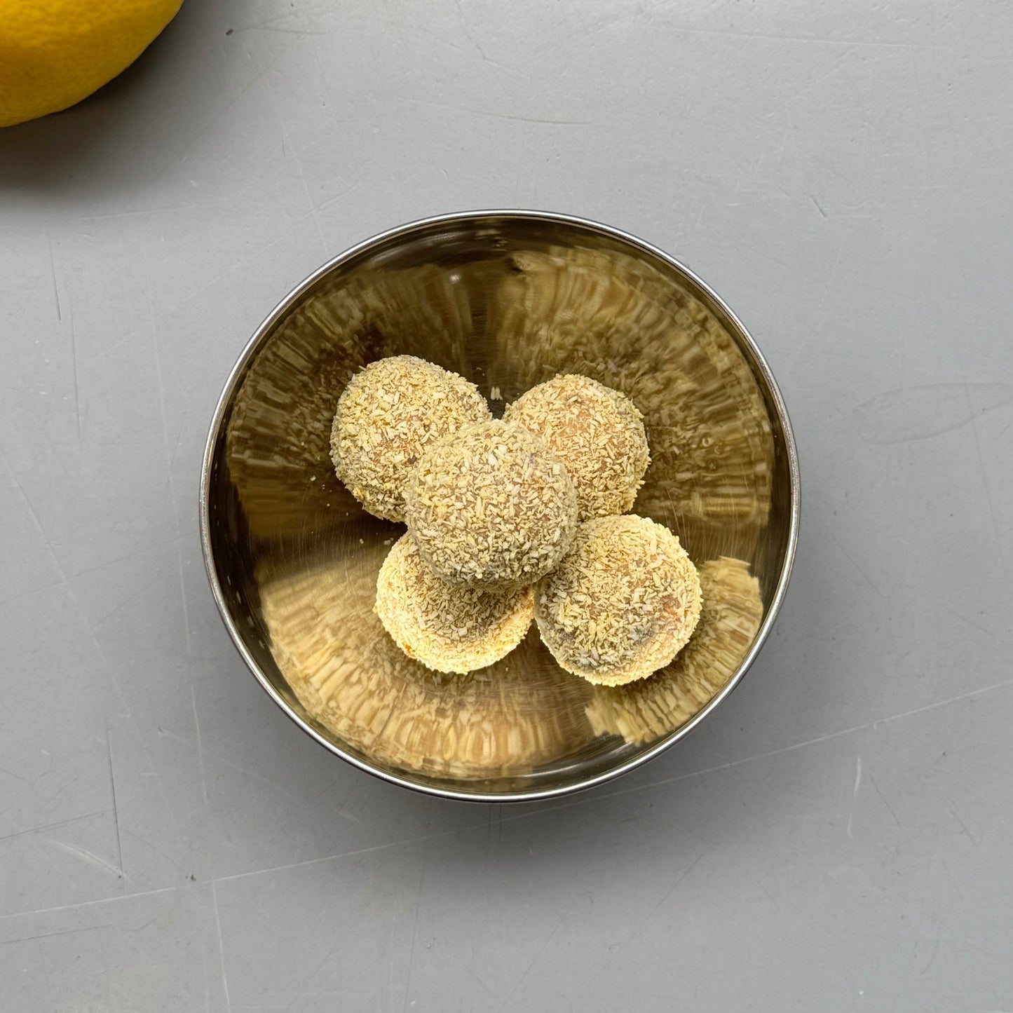 Metallic bowl with three round objects on a gray surface next to a lemon.
