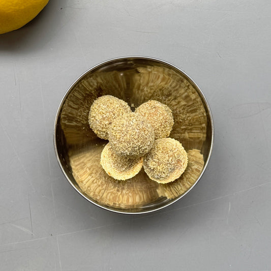 Metallic bowl with three round objects on a gray surface next to a lemon.