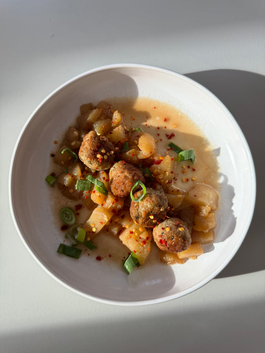A bowl of ginger chicken meatballs in pear sauce, garnished with basil leaves.