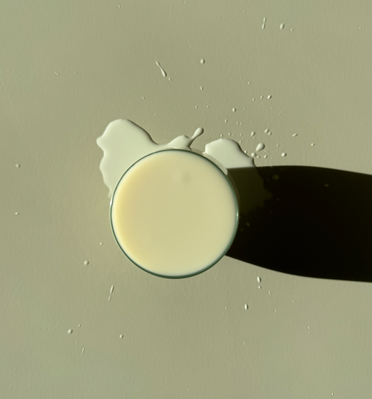 A glass of milk with a shadow cast on a beige background.