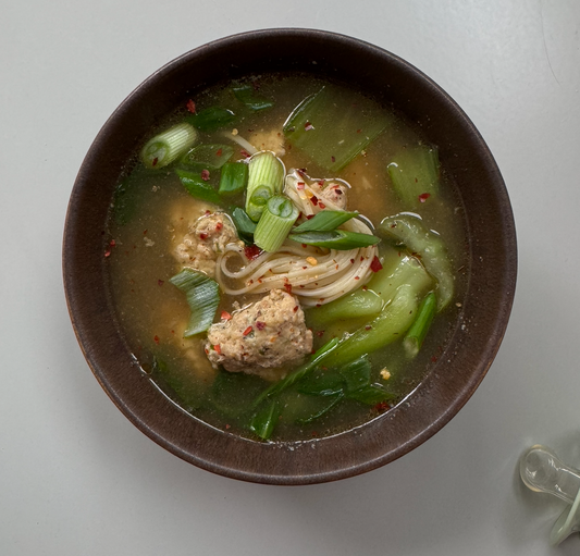 Bowl of soup with noodles, vegetables, and meatballs on a white background