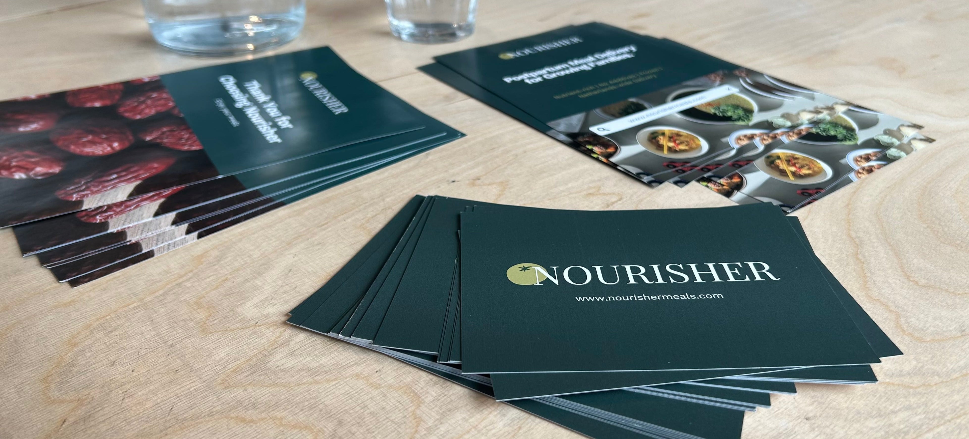 Nourisher business cards on a wooden surface with water glasses in the background