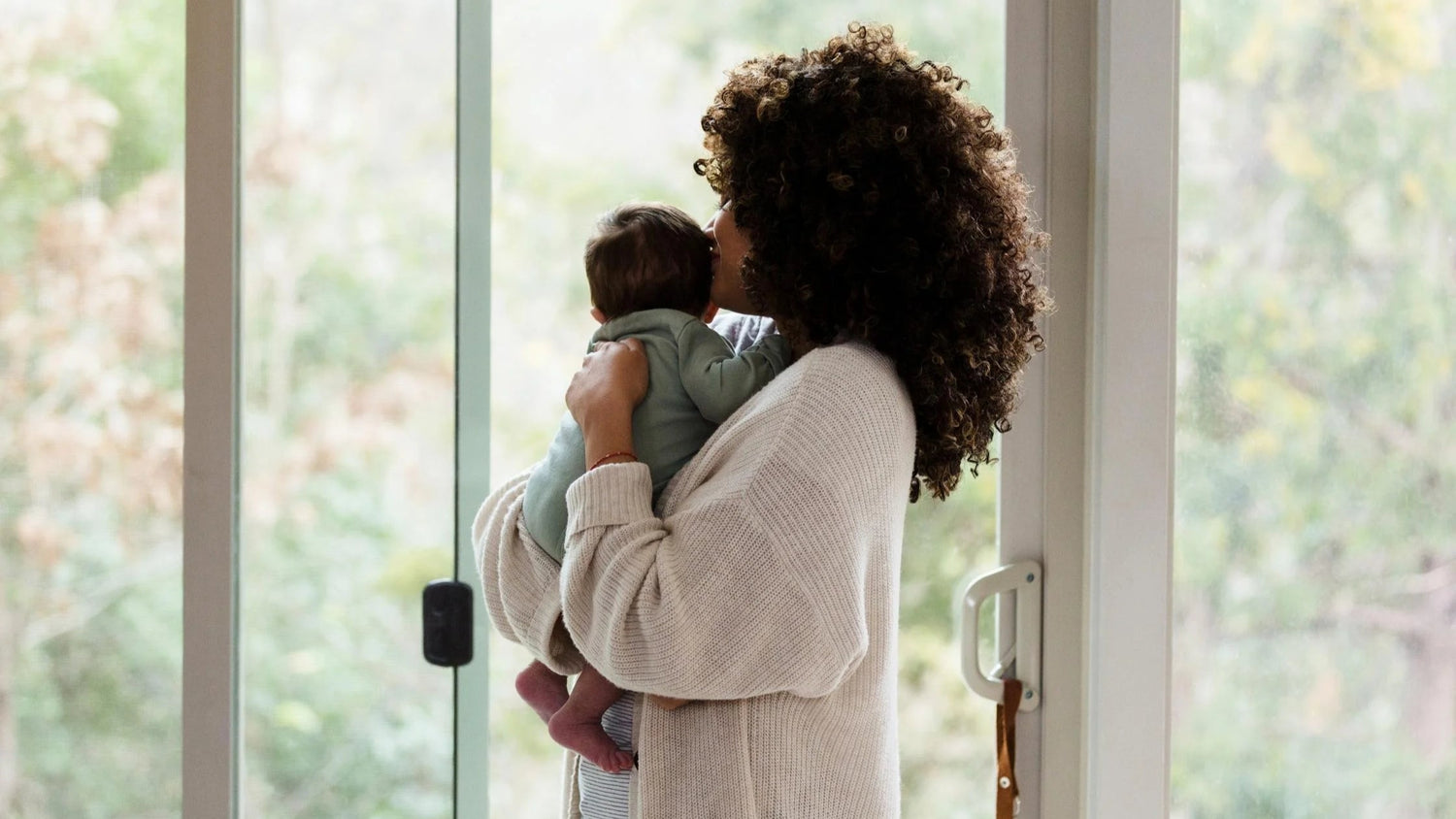 Woman holding a child by a window, looking out.