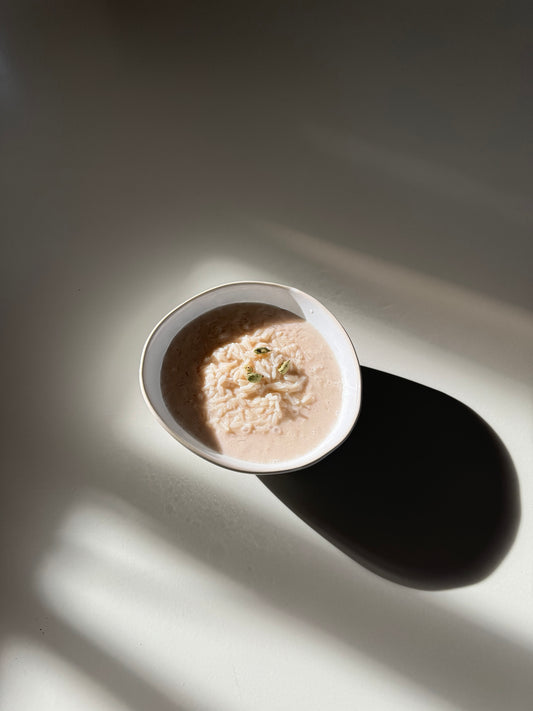 A bowl of Shatavari Rice Pudding on a light background with a shadow cast over part of the image.