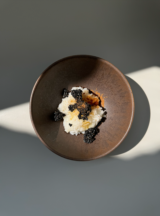 A bowl of Honey Congee with Black Sesame, with the congee and sesame seeds visible on the surface of the bowl.